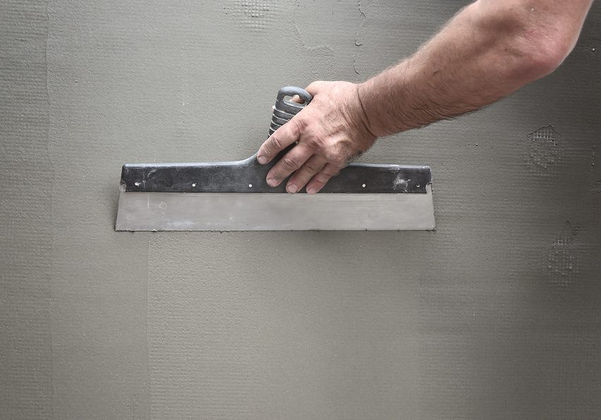 Hands of an old manual worker with wall plastering tools renovating house. Plasterer renovating outdoor walls and corners with spatula and plaster. Wall insulation. Construction finishing works